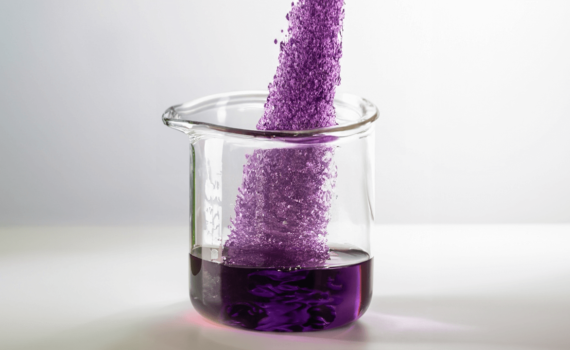 Permanganato de potássio cristalizado sendo despejado em béquer de vidro.