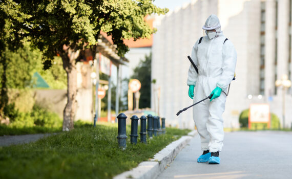 Homem em traje de proteção realizando a esterilização das ruas da cidade